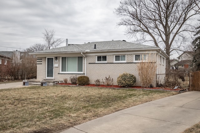 view of front of house featuring brick siding, fence, a front lawn, and roof with shingles