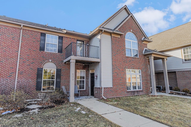 traditional-style home with brick siding, a balcony, and a front lawn