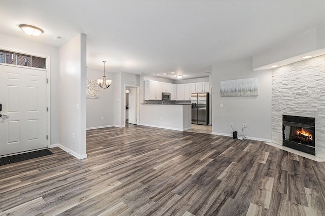 unfurnished living room featuring dark wood finished floors, a fireplace, baseboards, and an inviting chandelier