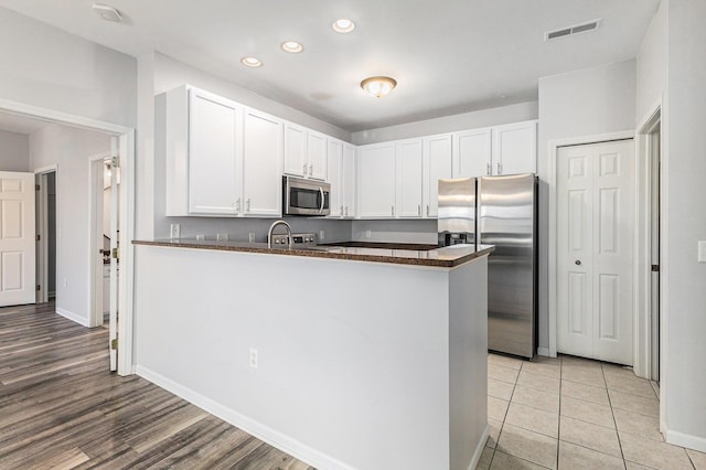 kitchen with stainless steel appliances, dark countertops, a peninsula, and visible vents