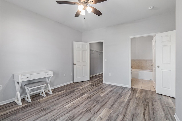 unfurnished bedroom featuring a ceiling fan, connected bathroom, baseboards, and wood finished floors