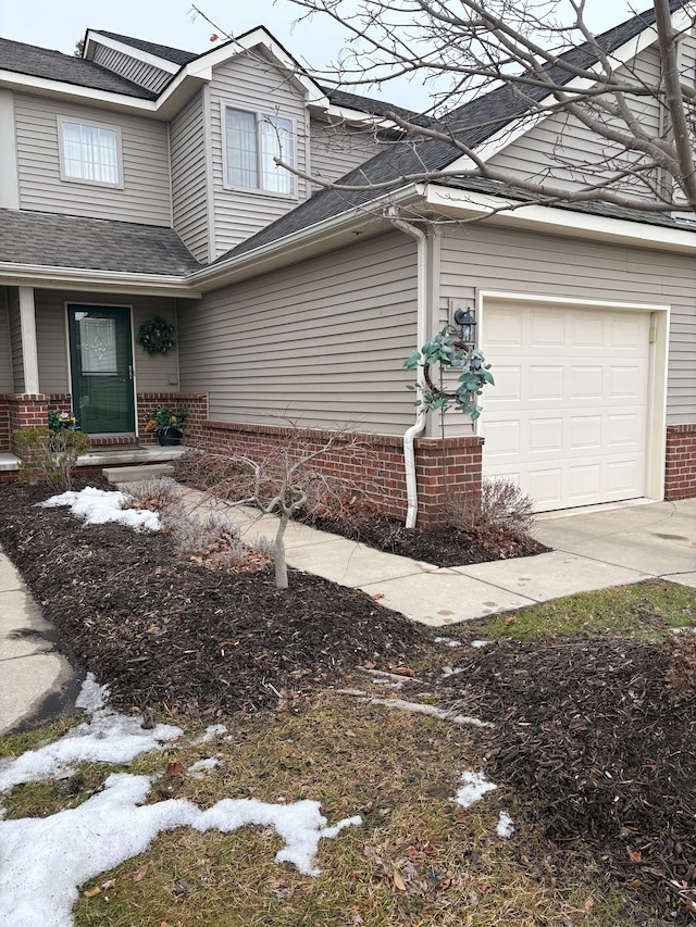 exterior space with a garage, driveway, a shingled roof, and brick siding