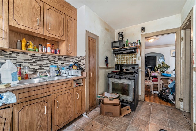 kitchen with open shelves, under cabinet range hood, stone finish flooring, decorative backsplash, and stainless steel gas range