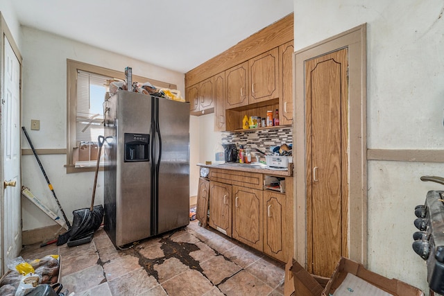 kitchen with tasteful backsplash, stainless steel fridge with ice dispenser, light countertops, stone finish floor, and a sink