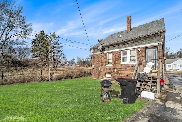 rear view of property with a shingled roof, a yard, brick siding, and a chimney