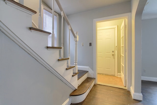 stairway with arched walkways, baseboards, and wood finished floors