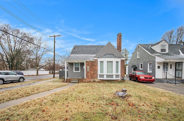 view of front of home with roof with shingles, brick siding, a chimney, and a front yard