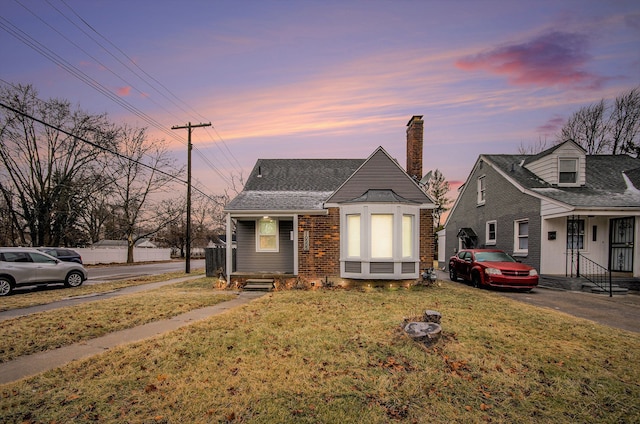 view of front of property featuring brick siding, a chimney, and a yard