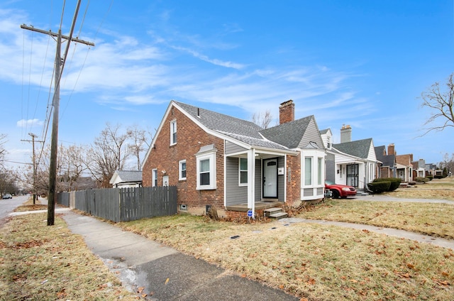 view of front of home with a front yard, brick siding, fence, and a chimney