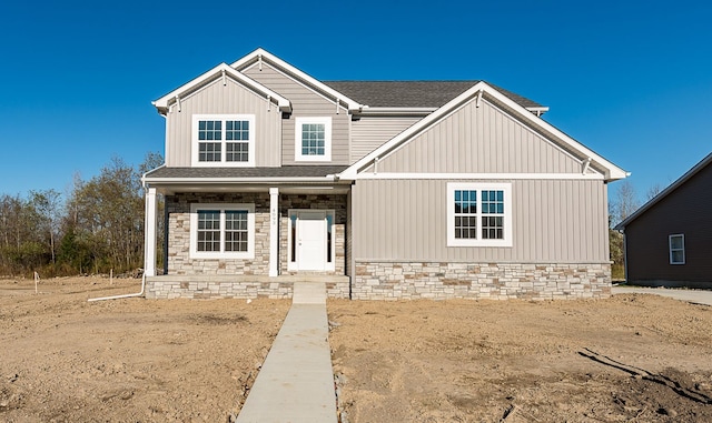 view of front facade with stone siding, a shingled roof, and board and batten siding