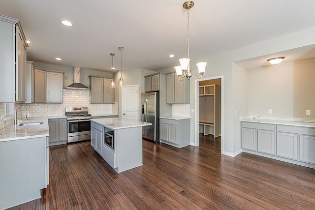 kitchen featuring gray cabinetry, dark wood-style flooring, a sink, appliances with stainless steel finishes, and wall chimney range hood