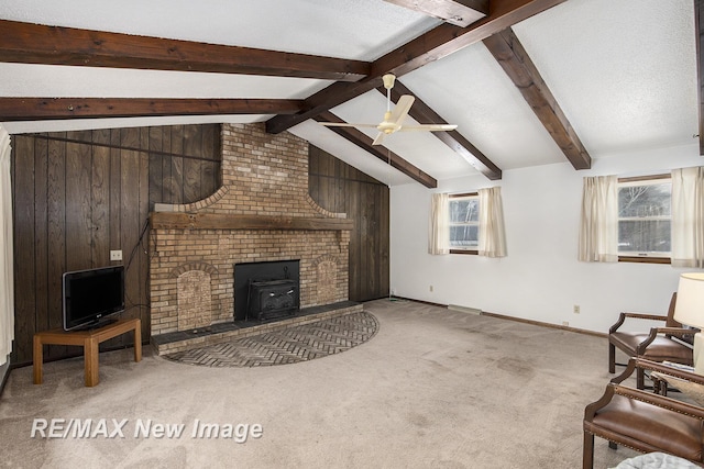 living room with carpet floors, vaulted ceiling with beams, a wood stove, and a wealth of natural light