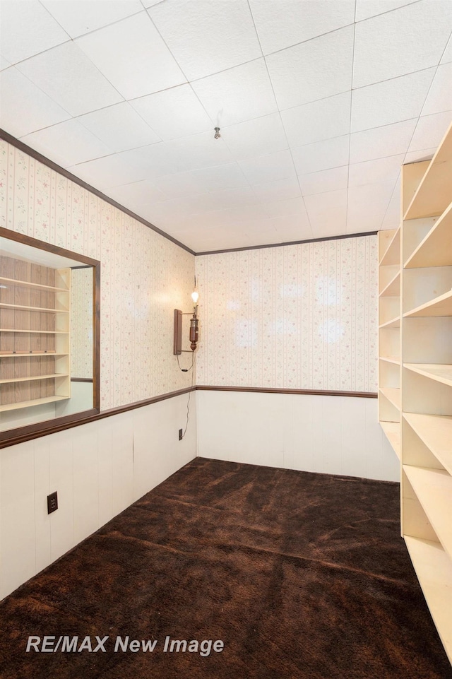 empty room with a wainscoted wall, crown molding, carpet flooring, and wallpapered walls