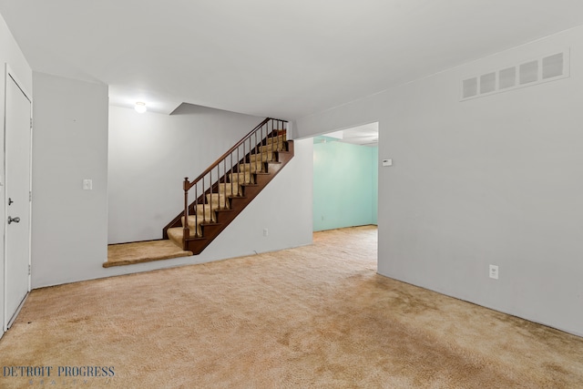 finished basement with visible vents, stairway, and carpet flooring