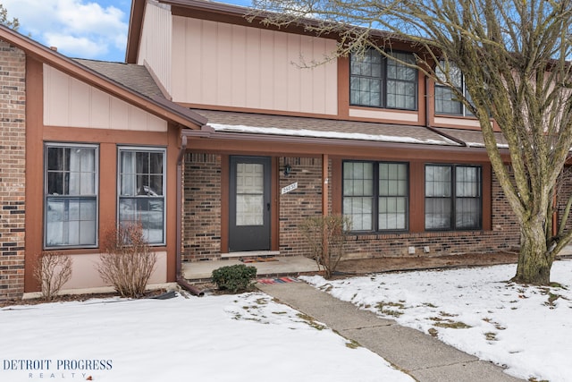 snow covered property entrance with brick siding and roof with shingles