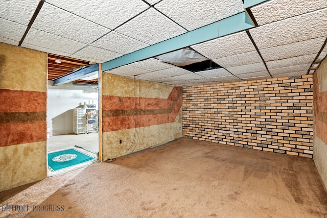 finished below grade area with a paneled ceiling, brick wall, and carpet flooring