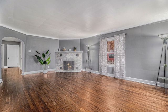 unfurnished living room featuring baseboards, a fireplace, arched walkways, and wood finished floors