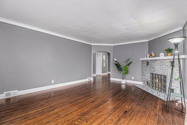 unfurnished living room with arched walkways, a fireplace, visible vents, wood finished floors, and baseboards