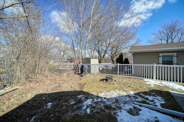 snowy yard featuring a storage shed, an outdoor fire pit, fence, and an outbuilding