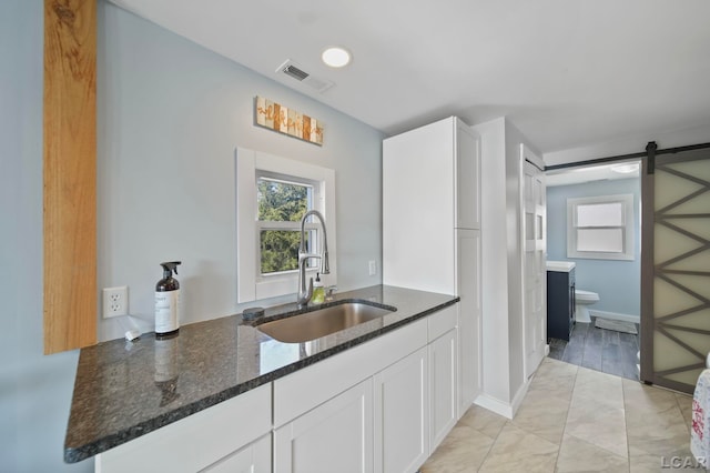 kitchen featuring a barn door, a sink, visible vents, white cabinetry, and dark stone counters