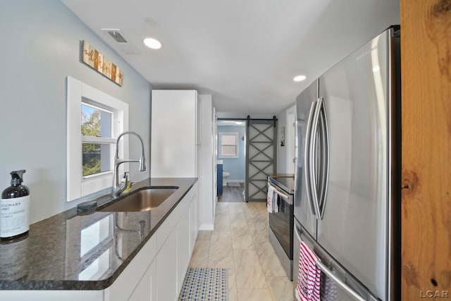 kitchen featuring a barn door, white cabinets, dark stone counters, appliances with stainless steel finishes, and a sink