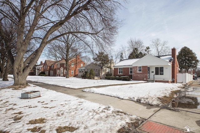 view of front of house featuring brick siding, a chimney, fence, and a residential view