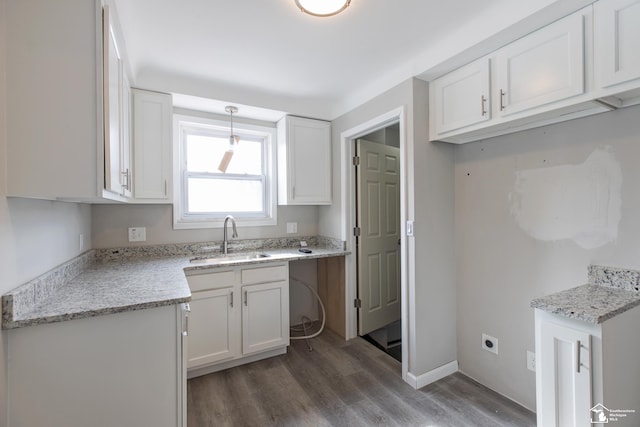 kitchen featuring white cabinets, wood finished floors, light stone countertops, pendant lighting, and a sink