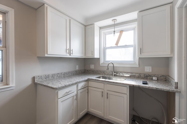 kitchen with a sink, white cabinetry, and light stone countertops