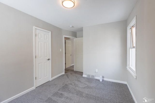 unfurnished bedroom with carpet floors, visible vents, multiple windows, and baseboards