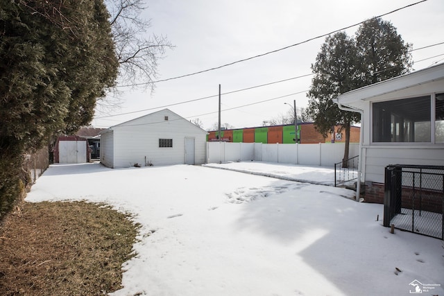 yard layered in snow with a sunroom, fence, and an outbuilding