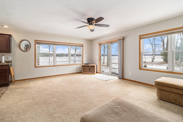 living area featuring light carpet, ceiling fan, baseboards, and a textured ceiling