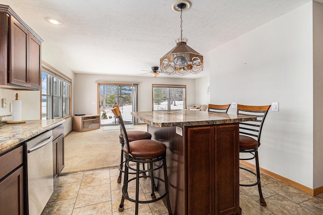 kitchen with a textured ceiling, a kitchen breakfast bar, stainless steel dishwasher, and decorative light fixtures