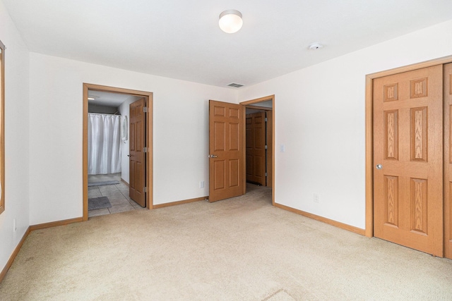 unfurnished bedroom featuring baseboards, ensuite bath, visible vents, and light colored carpet