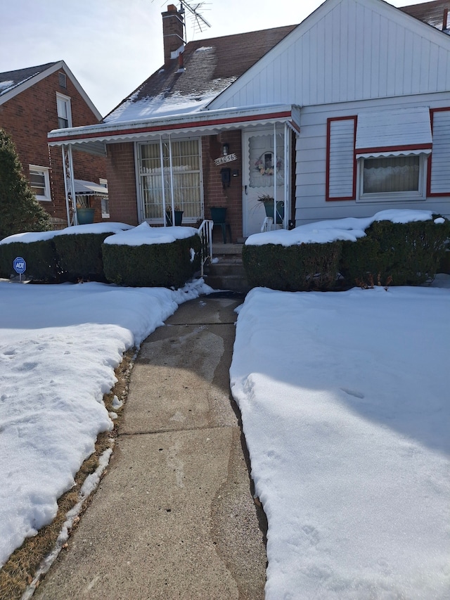 view of front of property featuring covered porch, brick siding, and a chimney