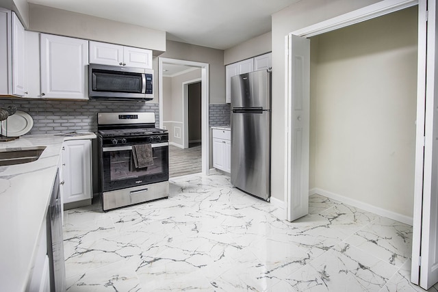 kitchen with baseboards, white cabinets, marble finish floor, stainless steel appliances, and a sink