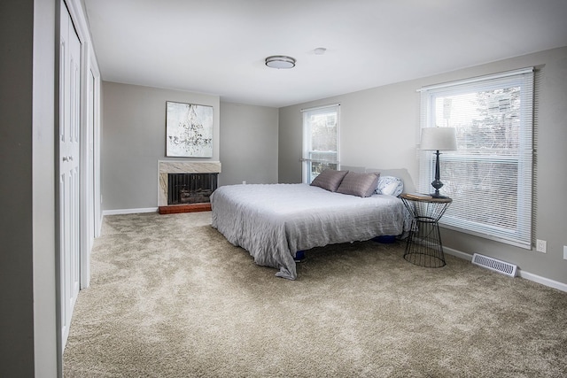 bedroom with carpet, visible vents, a fireplace with raised hearth, and baseboards