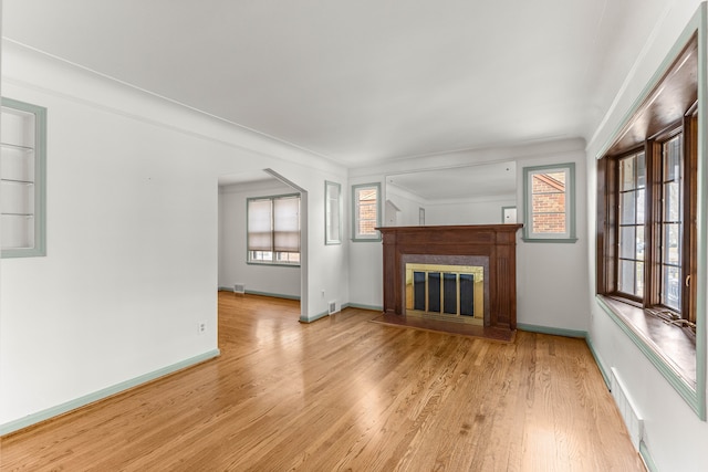 unfurnished living room with visible vents, baseboards, ornamental molding, light wood finished floors, and a glass covered fireplace