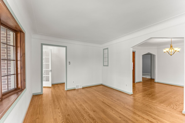 empty room with arched walkways, light wood-style flooring, visible vents, baseboards, and an inviting chandelier