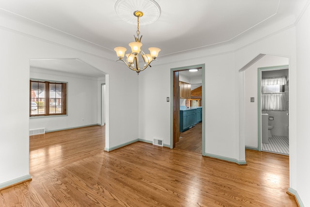 unfurnished dining area featuring arched walkways, visible vents, a notable chandelier, and wood finished floors