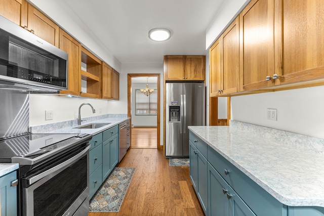 kitchen featuring wood finished floors, a sink, appliances with stainless steel finishes, open shelves, and an inviting chandelier