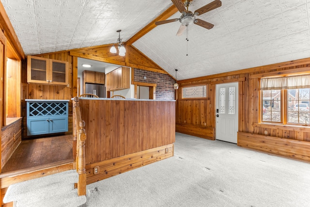 kitchen with light carpet, lofted ceiling with beams, ceiling fan, stainless steel refrigerator, and wood walls