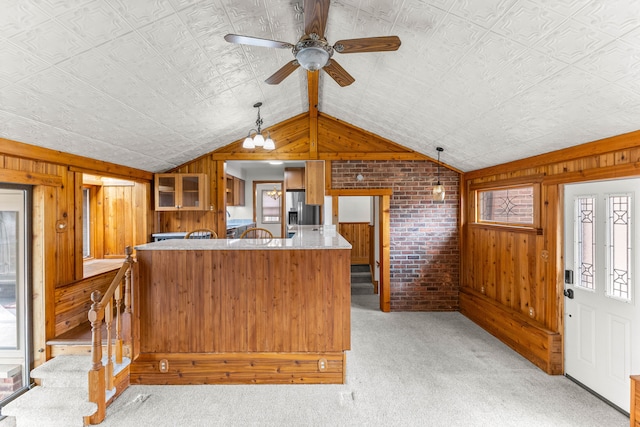 kitchen with pendant lighting, stainless steel refrigerator with ice dispenser, lofted ceiling, light colored carpet, and wood walls