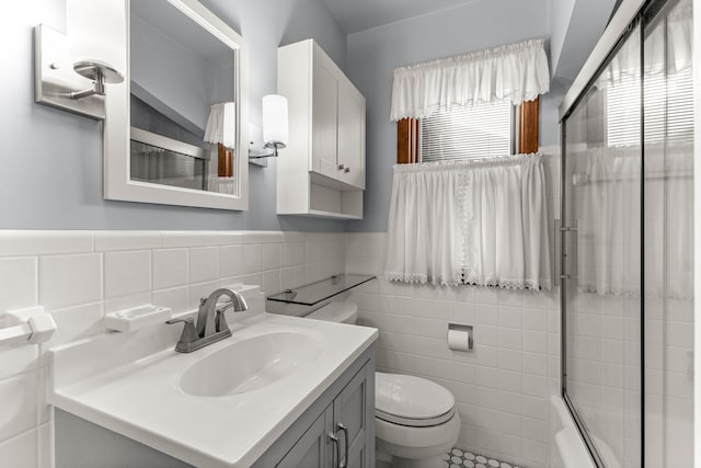 full bath featuring toilet, a wainscoted wall, vanity, tile walls, and combined bath / shower with glass door