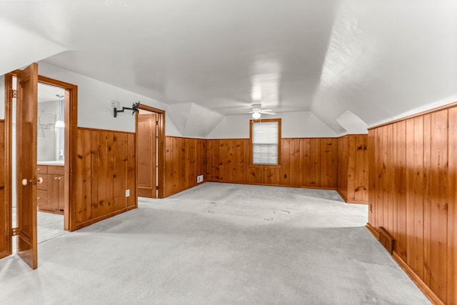 bonus room featuring lofted ceiling, light colored carpet, a ceiling fan, wainscoting, and wooden walls