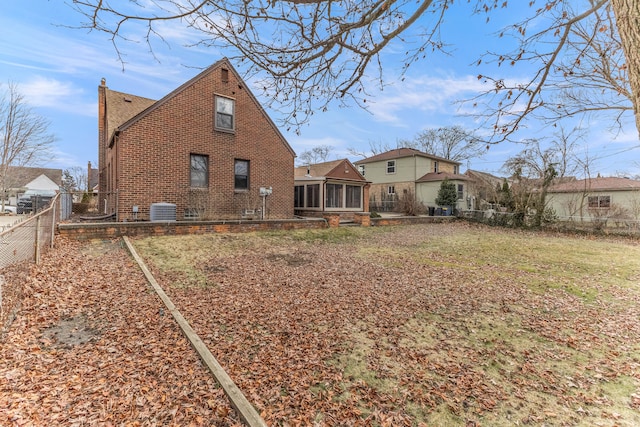 back of house featuring cooling unit, brick siding, fence, a sunroom, and a chimney