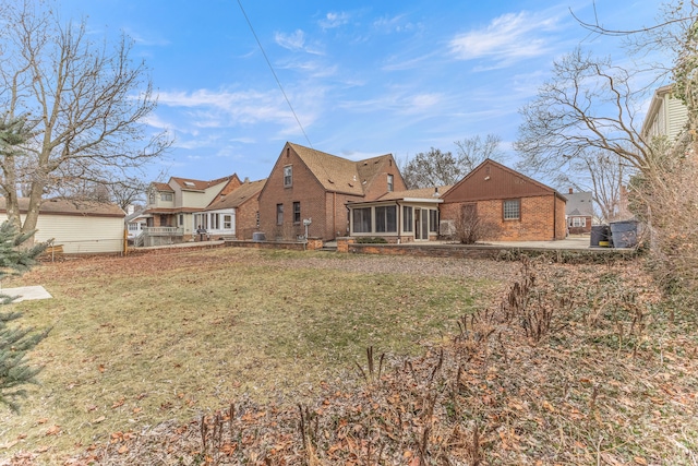 back of property featuring a sunroom, a lawn, and brick siding