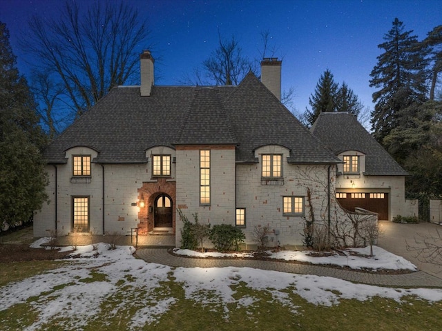 french country style house featuring a garage, stone siding, driveway, and a chimney