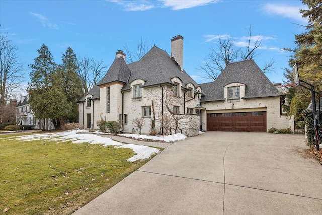 french country home with driveway, stone siding, a chimney, and a front yard