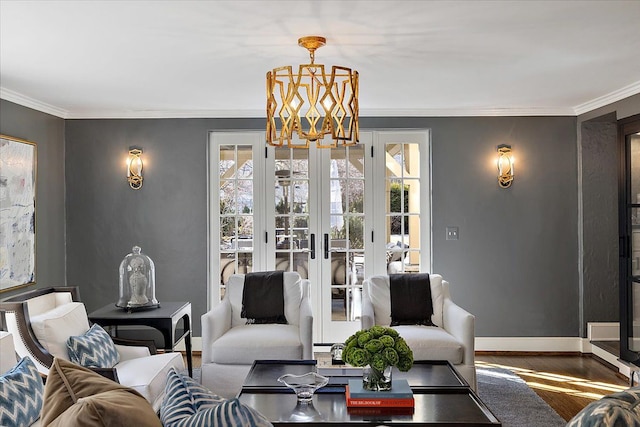 living area with baseboards, ornamental molding, a chandelier, and wood finished floors