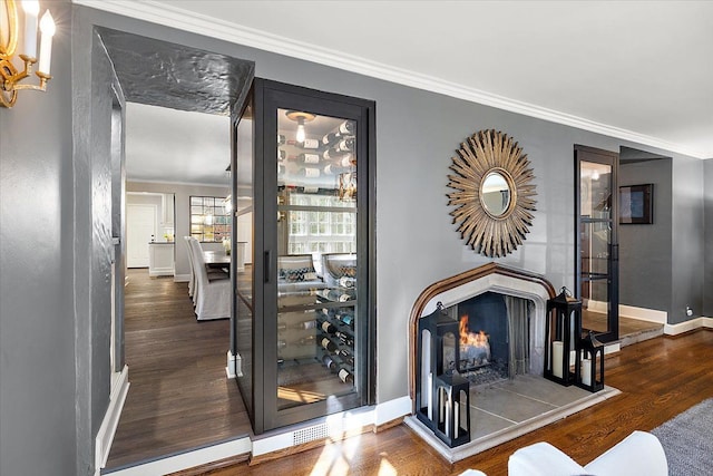 interior space with a warm lit fireplace, baseboards, ornamental molding, and wood finished floors